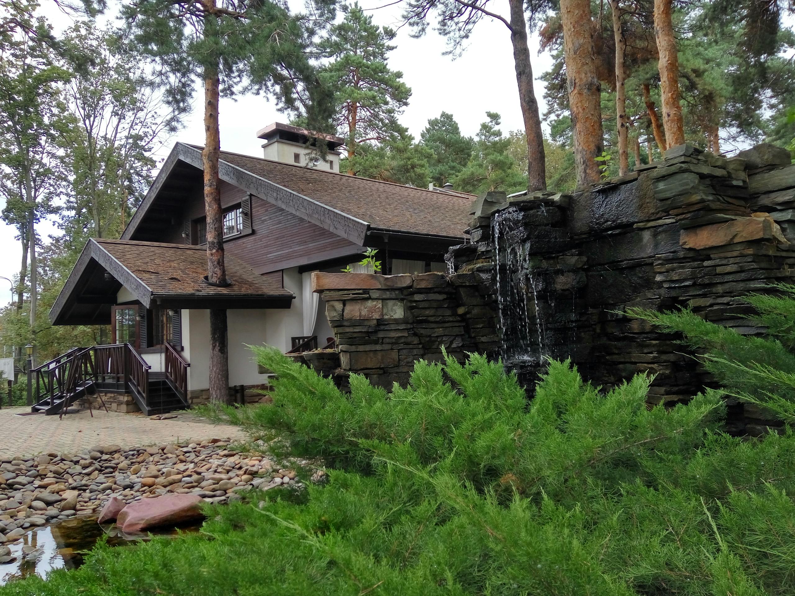 A picturesque modern rural house surrounded by greenery and a cascading waterfall in a serene outdoor setting.