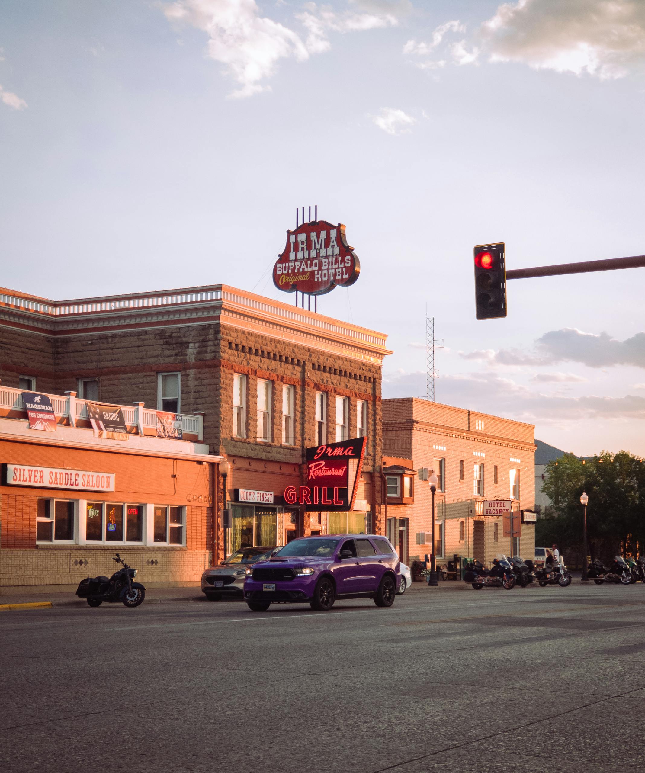 Sunset view of a historic hotel and street with parked vehicles and moving cars.